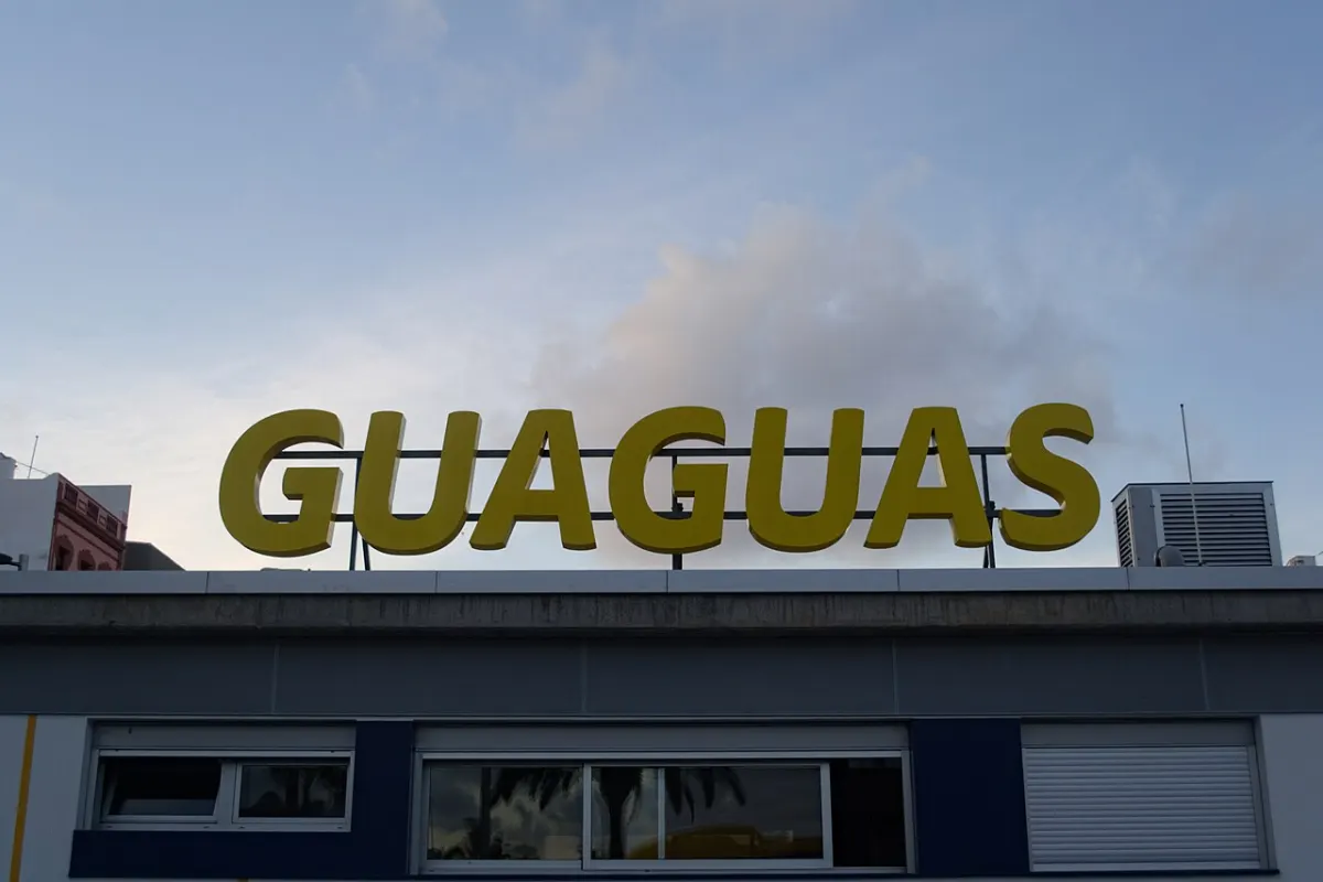 Große gelbe Buchstaben „GUAGUAS“ stehen auf dem Dach eines flachen Gebäudes vor bewölktem Himmel.